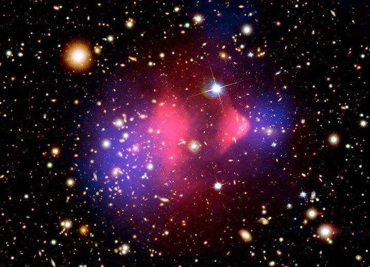 Two galaxy clusters after a collision, with the mass (blue) separated from the visible matter (pink). It is among the clearest evidence that dark matter exists, and among the least informative about what it actually is (Credit : X-ray NASA/CXC/CfA/M. Markevitch et al.; Optical NASA/STScI; Lensing map NASA/STScI, ESO WFI, Magellan/U.Arizona/D. Clowe et al.)