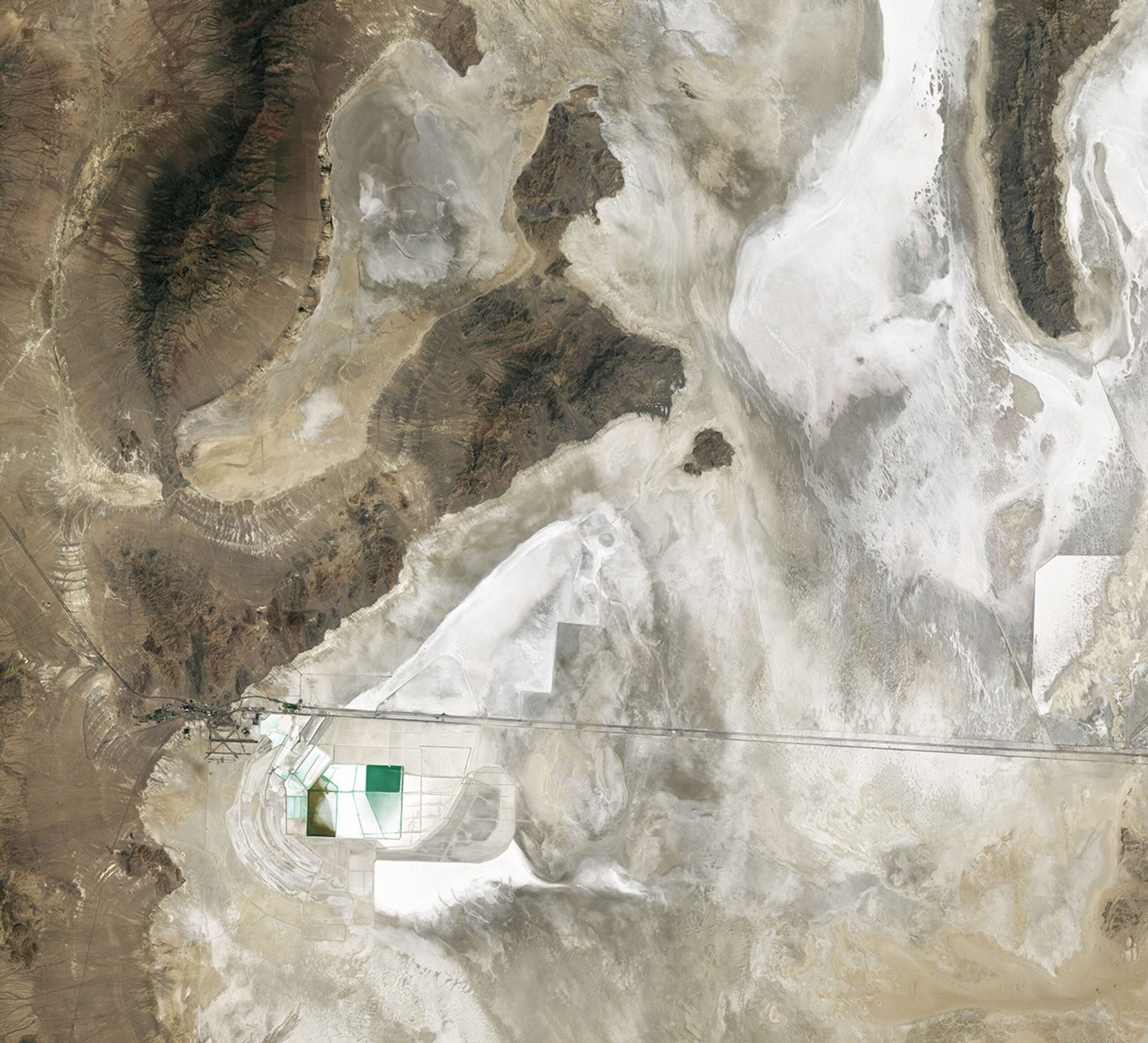 A nadir view shows Crater Island—a dark, linear mountain ridge in the center of the image—flanked by flat tan and white landscapes.