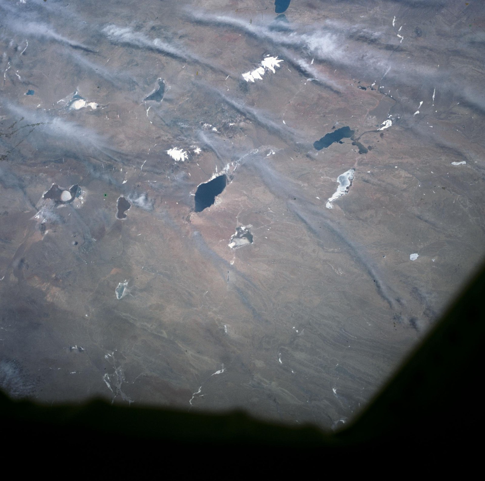 View of Earth from orbit showing whispy clouds and a landscape dotted with lakes.