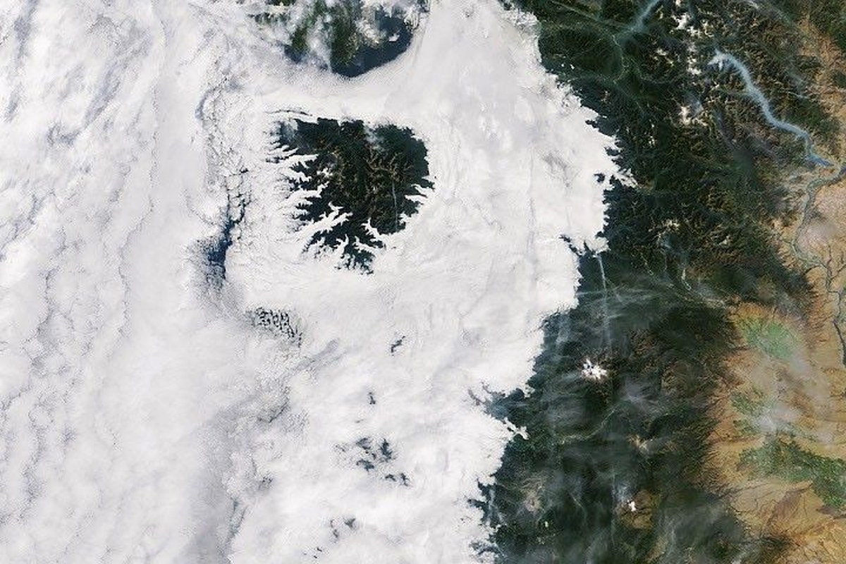 Low-lying clouds cover western Washington and Oregon between the Pacific coast and the foothills of the Cascade Range. Parts of the Olympic Mountains and Oregon Coast Range are visible above the clouds.