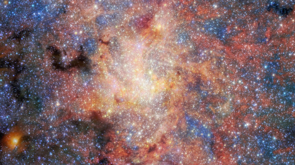 A scene of dust, gas and stars in red, orange, black and blue.