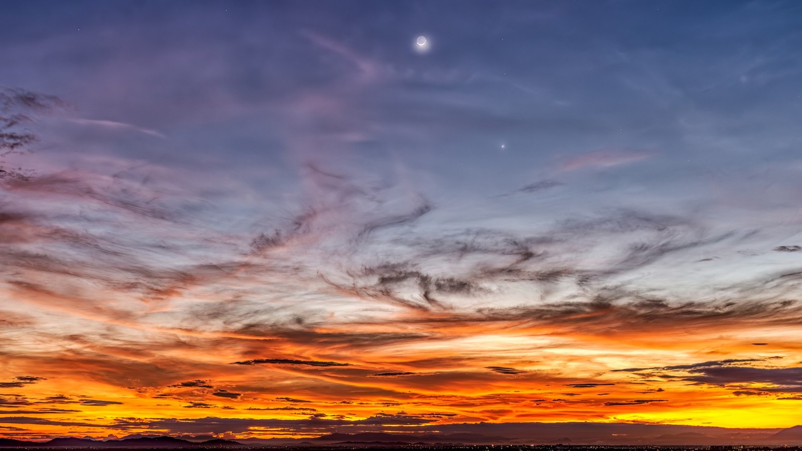 a fiery orange sunset sky with the moon upper center and Venus to the lower right.