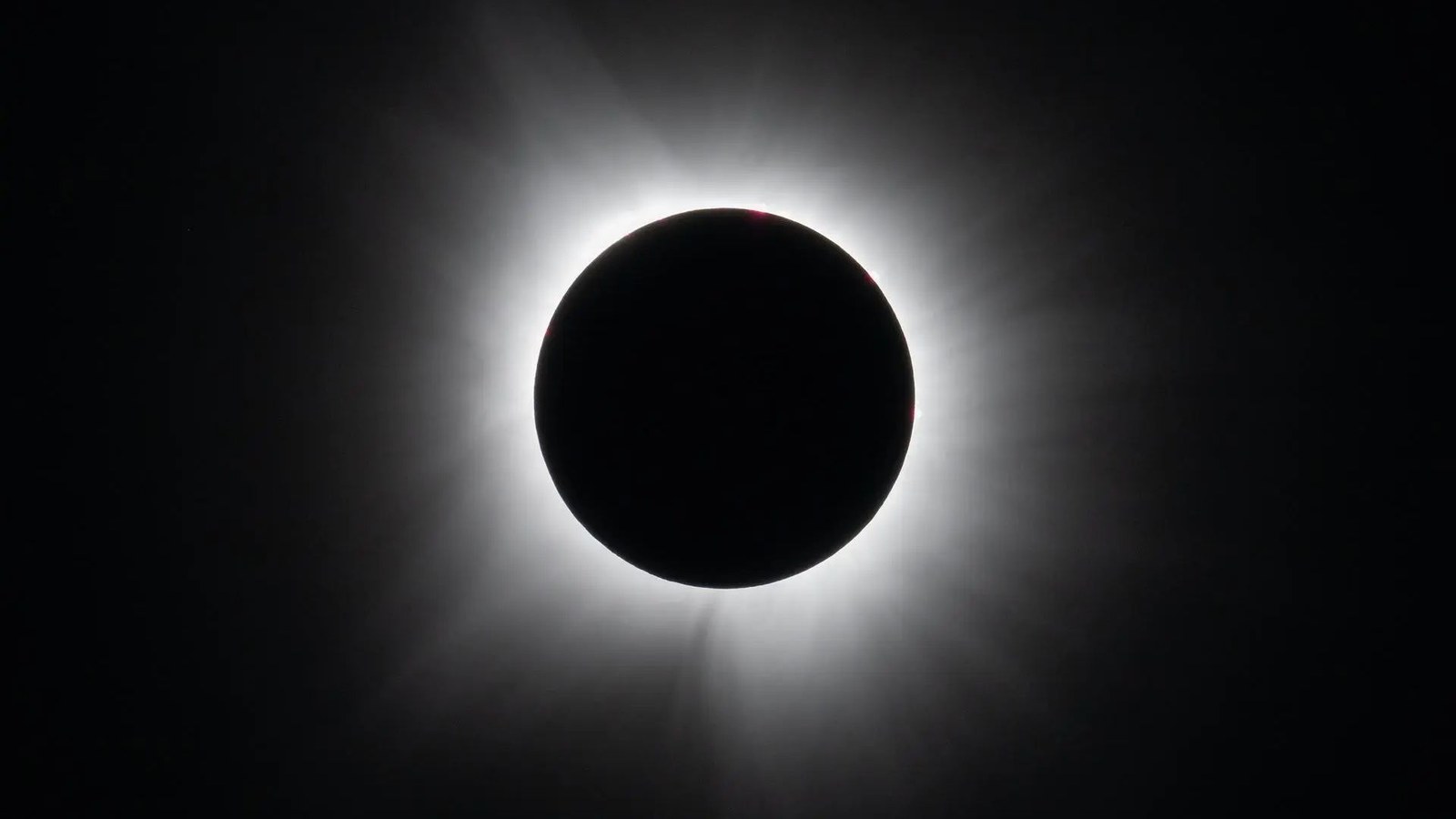 A black circle against a black background surrounded by white wispy tendrils