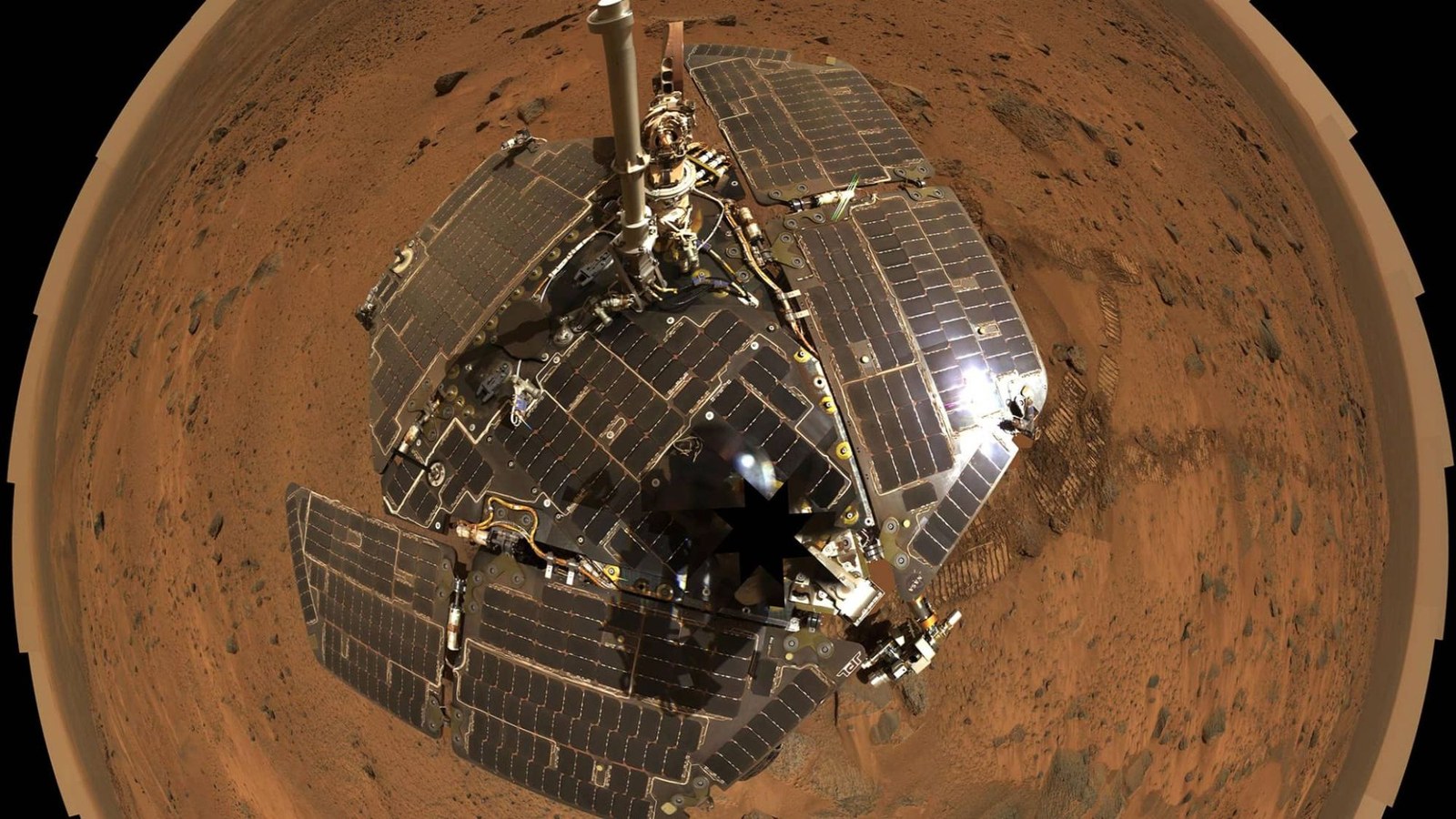 A fisheye view of a solar paneled rover on a reddish terrain.