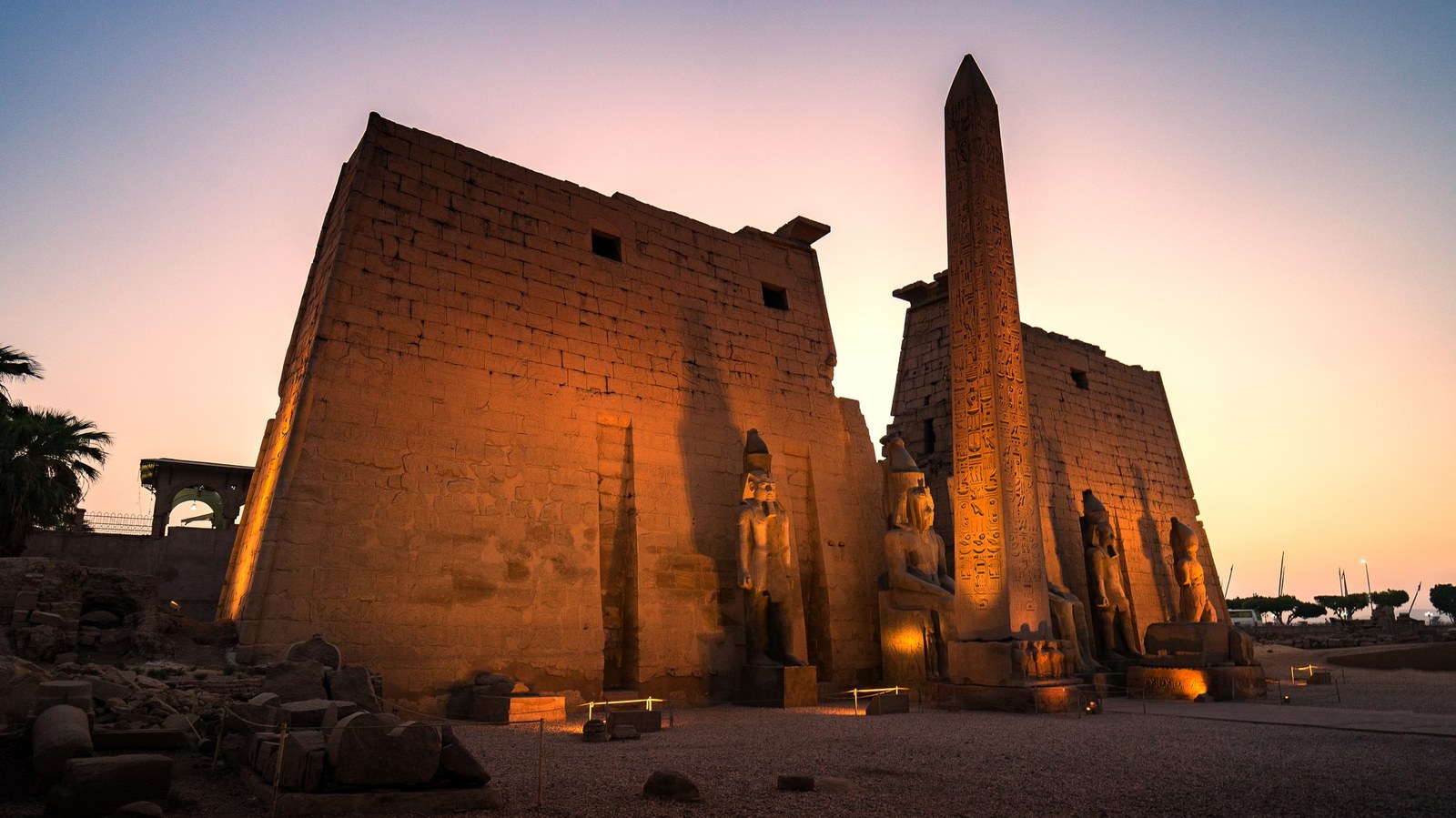 Beautiful sunset at Ruins Luxor temple and obelisk near Nile river at Luxor city Egypt. A tall structure is backlit from a rising sun.