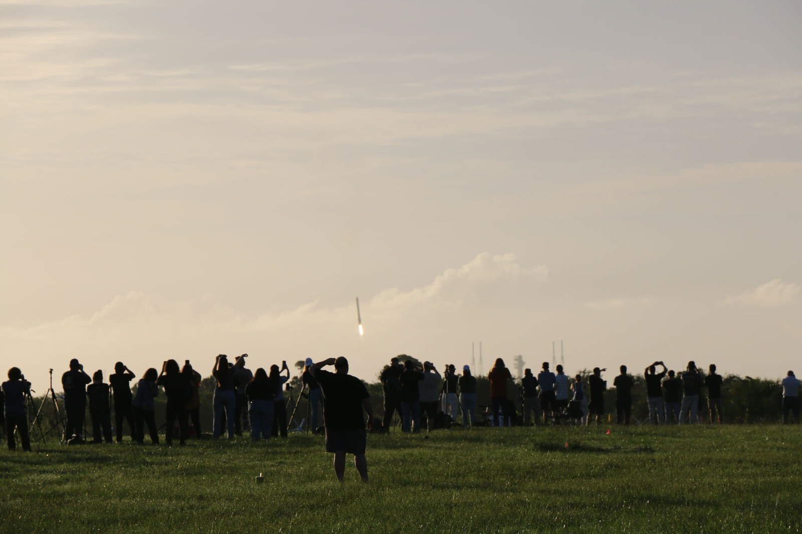 People stand on a lawn watching a long structure descend to Earth.