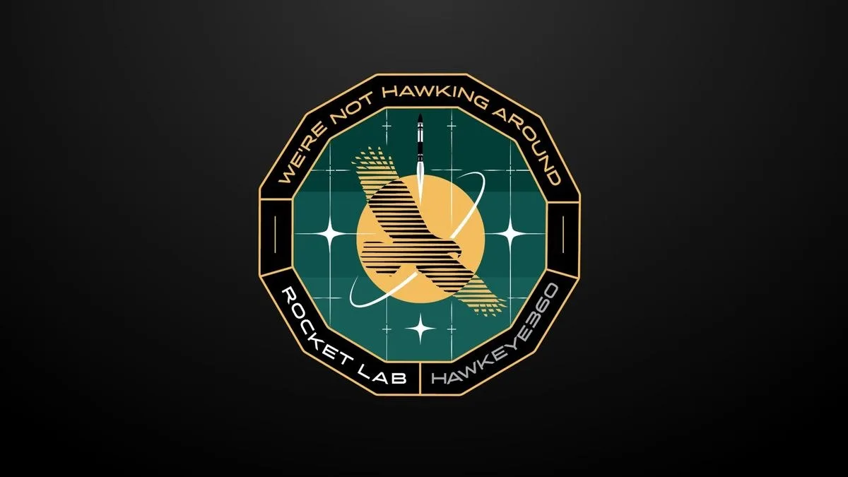 a circular mission patch featuring a hawk in front of a yellow sun with the words "We're Not Hawking Around" around the patch's border