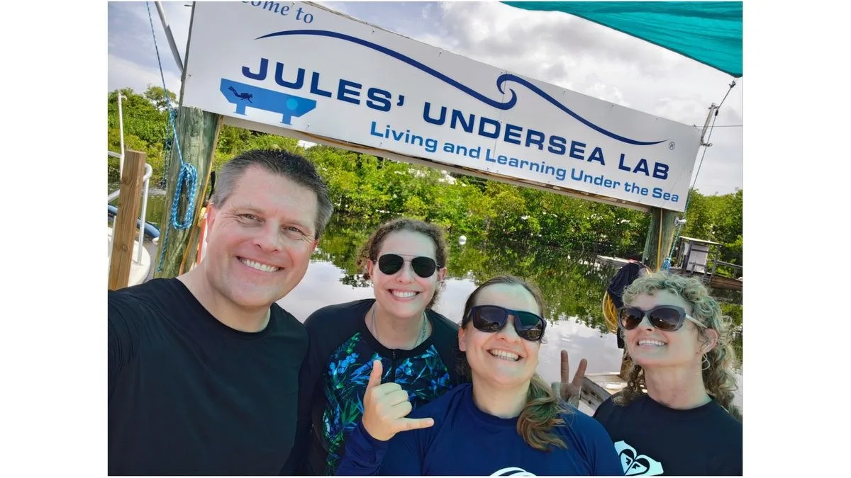 photo of four smiling people, three women and one man, standing outside by a sign that reads "jules' undersea lab"