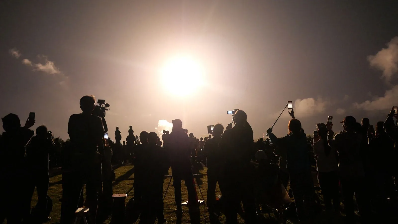 A photo of a crowd watching a rocket launch at night